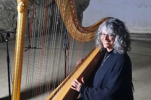 Woman in long black dress smiling and shouldering large harp, about to play