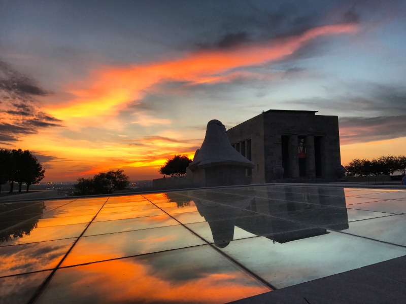 Brilliant flame-colored evening sky and stone building in classical style reflected in mirror panels on ground in front of the building