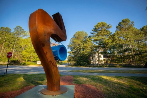 Large abstract sculpture in park, rust-colored S-curved upright with blue circle handing from the middle