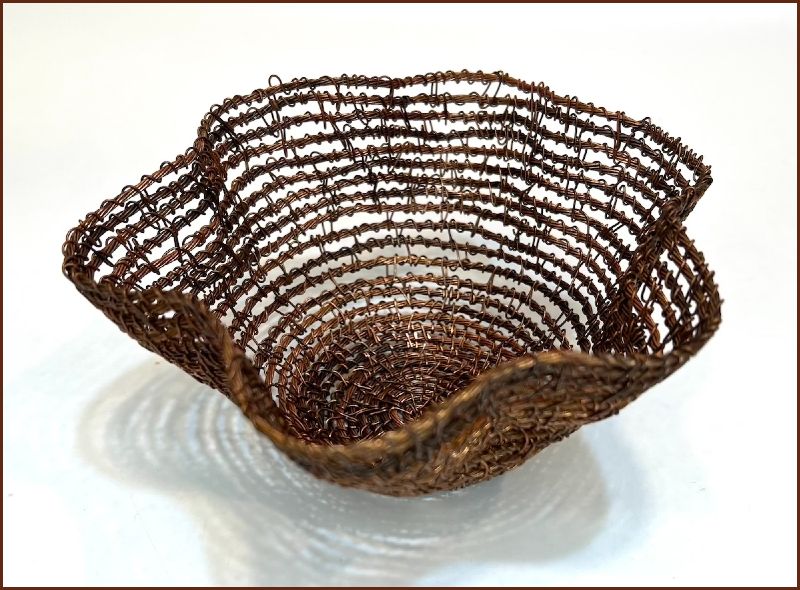 Open-weave basket made of thin strands of copper metal, wavy brim