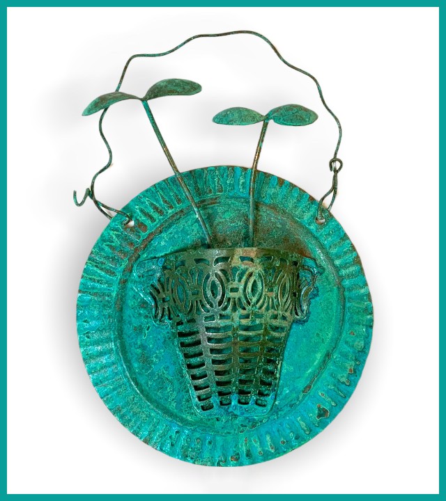 Wall hanging of round plate with half-vase on it and two sprouts coming out of the base, all in shades of turquoise