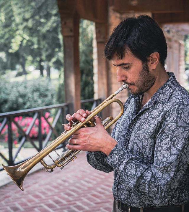 Man standing in garden portico, playing trumpet, seen in profile