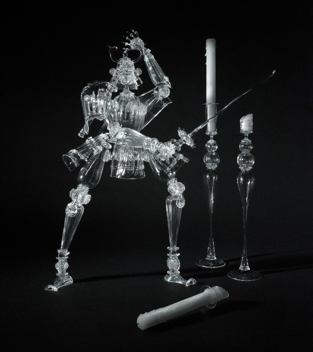 Glass figure created from stemware, in armor of ancient Asian warrior, holding sword and lopping off candles in nearby glass candleholders