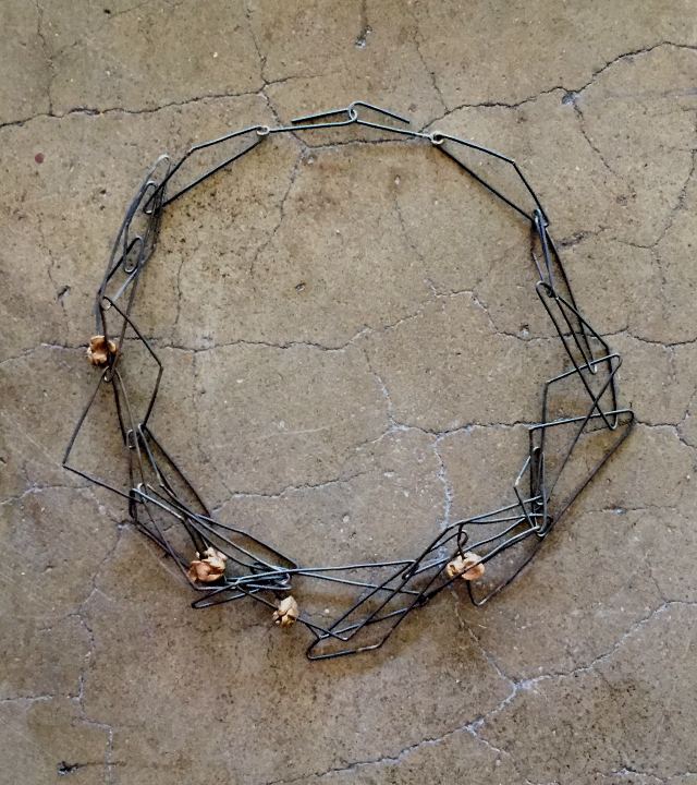 Necklace made of large triangular links of black steel interlaced with roughly textured bronze beads