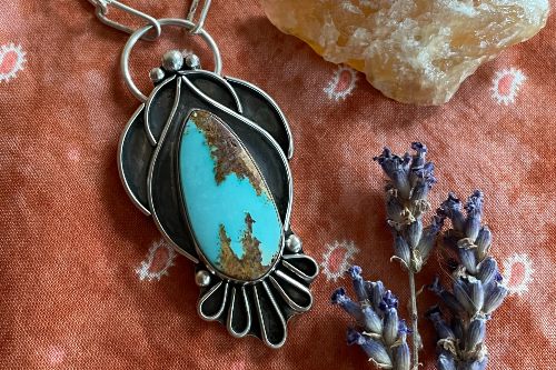 Photograph of close-up of pendant, oval turquoise stone with gold inclusions, set within silver and black curving shapes