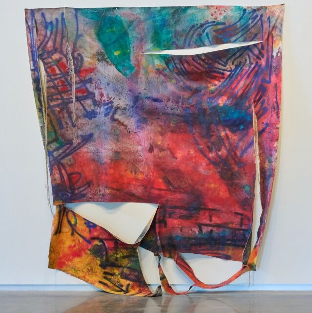 Large fabric sculpture on wall, flat square shape, with abstract designs in full spectrum of brilliant colors