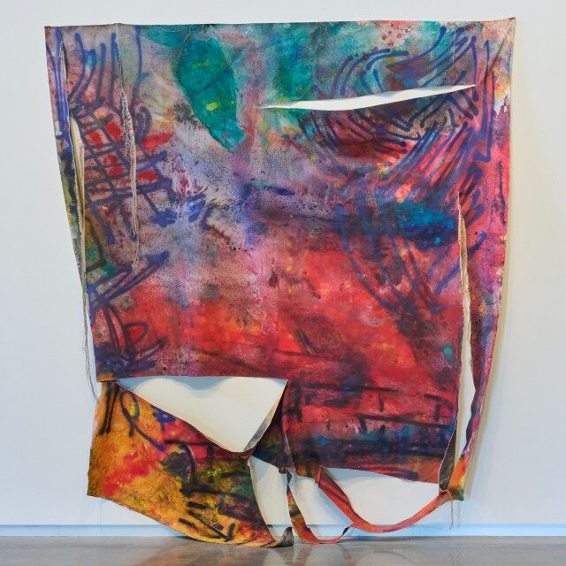 Large fabric sculpture on wall, flat square shape, with abstract designs in full spectrum of brilliant colors