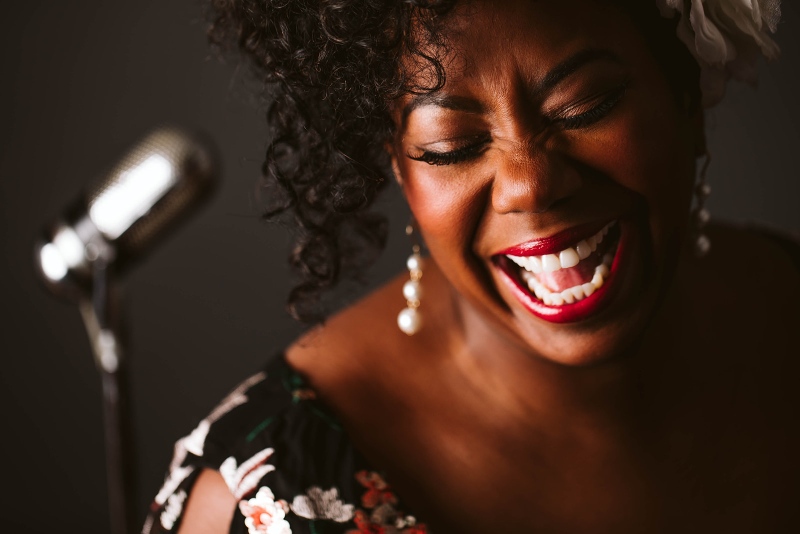 Close-up photo of woman singing joyously with microphone in background