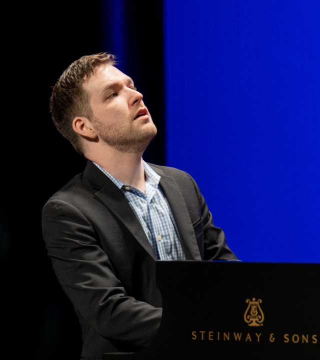 Man sitting at piano, from waist up, with words "Steinway & Sons" in gold on the black piano