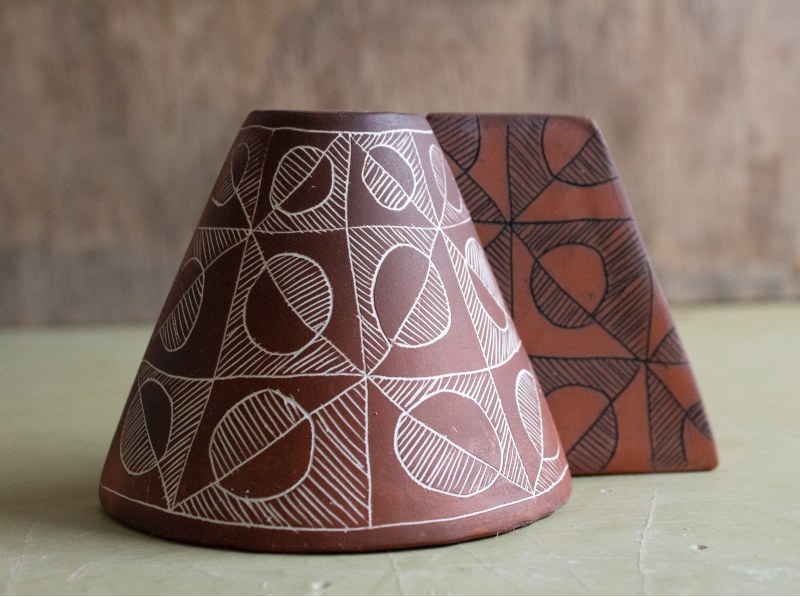 Two pieces of pottery in a cone shape with the top cut off, brick red color with white patterns on one and black patterns on the other, circles and squares accented by straight lines