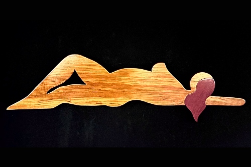 Two-dimensional abstract sculpture of a silhouette of a nude woman lying on her side, with her body in light brown wood and her hair in purple wood